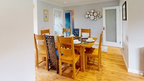 Uma sala de jantar com uma mesa de madeira posta para quatro pessoas, rodeada por cadeiras combinando.