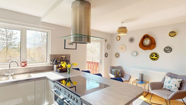 Cozinha moderna com ilha central, área de refeições com cadeira e mesa, e sala de estar com sofá e objetos decorativos na parede.