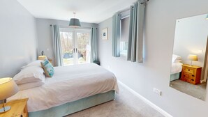 Quarto com cama, mesa de cabeceira, luminária, janela com cortinas e espelho.