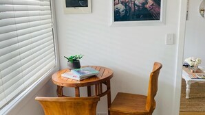 A corner room with a wooden table and two chairs, a potted plant, a framed painting, and a white door. -  Private Central Guesthouse (Dudley Park)