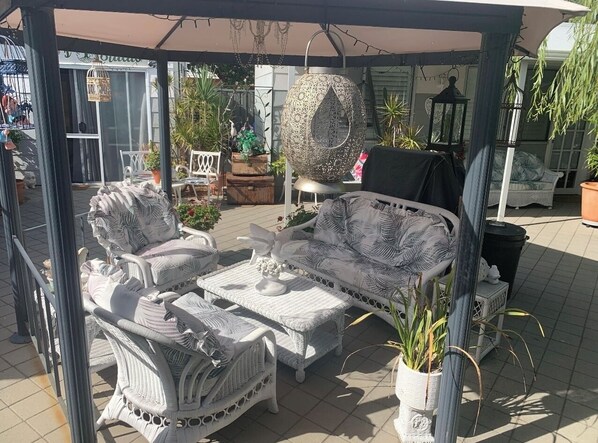 An outdoor patio area with wicker furniture, including a sofa and chairs, under a covered structure.