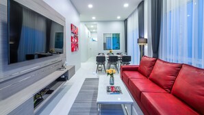 Un salon moderne doté d’un téléviseur à écran plat, d’un canapé en cuir rouge et d’un coin repas avec une table et des chaises.