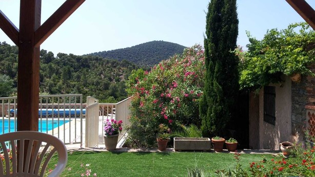 A covered patio with a view of a pool and a hillside.