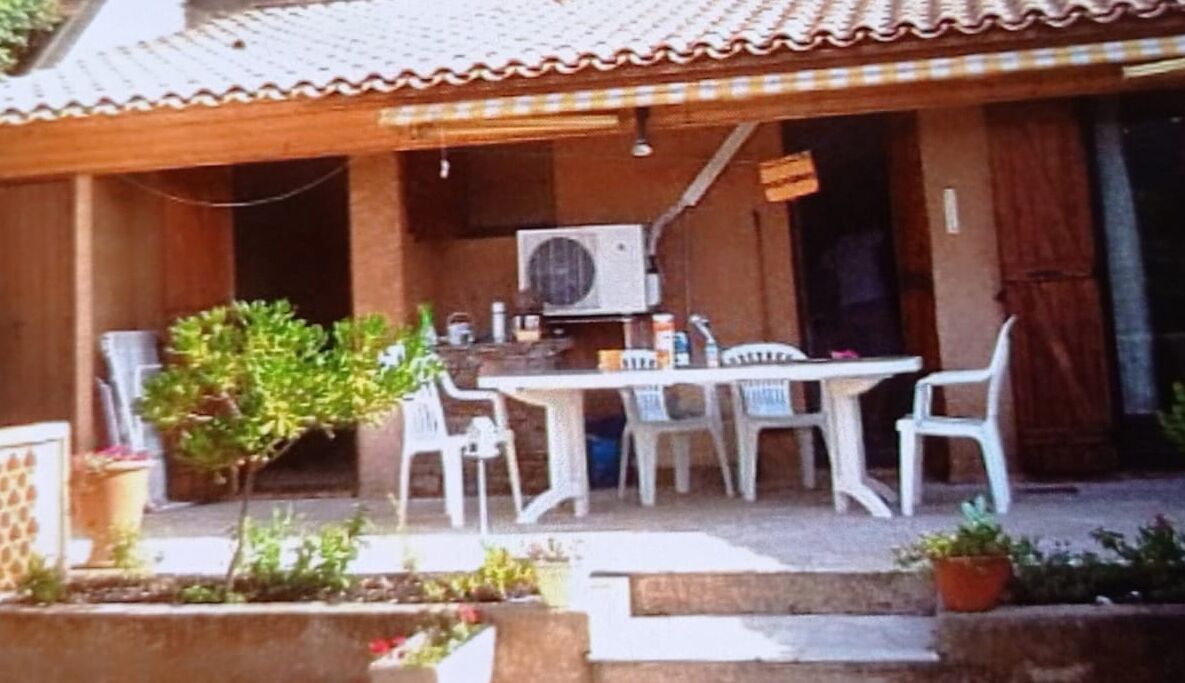 Un patio al aire libre con una mesa, sillas, un equipo de aire acondicionado y plantas en macetas.