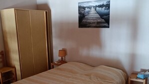 A bedroom with a bed, a wardrobe, a nightstand, a lamp, and a painting on the wall.