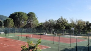 A tennis court with a net, surrounded by a fence and trees.