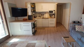 A compact living space with a kitchenette, a grey sofa, a TV, and a small table.