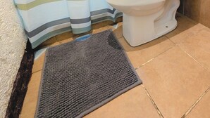 A bathroom with a striped shower curtain, a white toilet, and a dark mat on the floor. - Casa Quetzalli Los Nazarenos (Antigua Guatemala)