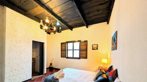 A bedroom with a bed, a chandelier, a window with shutters, and a painting on the wall. - Casa Quetzalli Los Nazarenos (Antigua Guatemala)