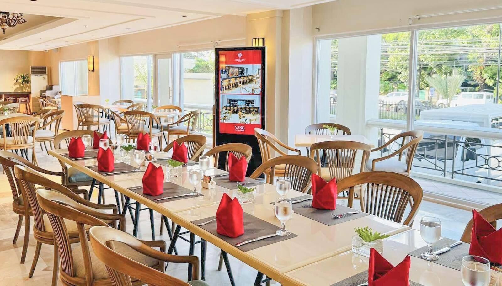 Un restaurante con mesas largas, sillas de madera y servilletas rojas.