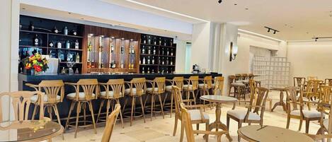 A bar area with shelves of bottles and a counter. There are multiple wooden chairs and tables arranged for seating.