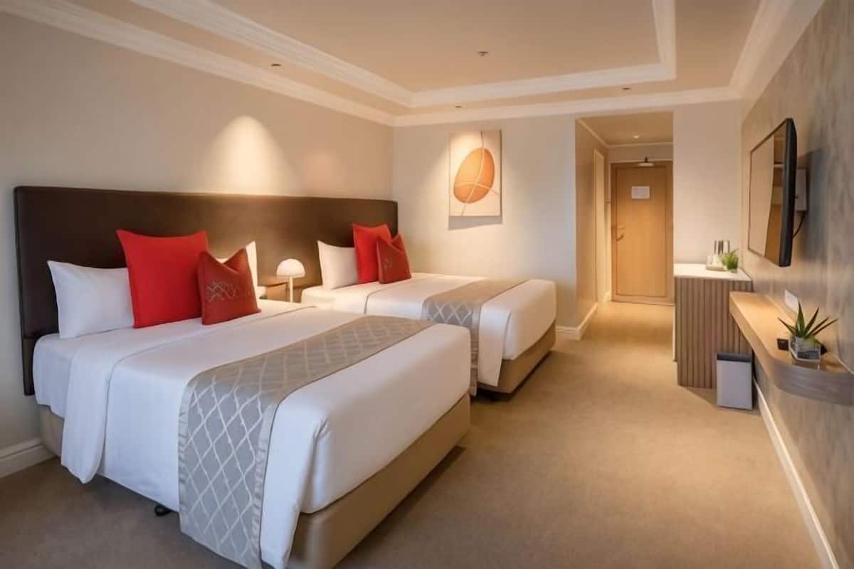 Une chambre d’hôtel avec deux lits, un bureau, un miroir et une porte donnant sur une autre pièce.