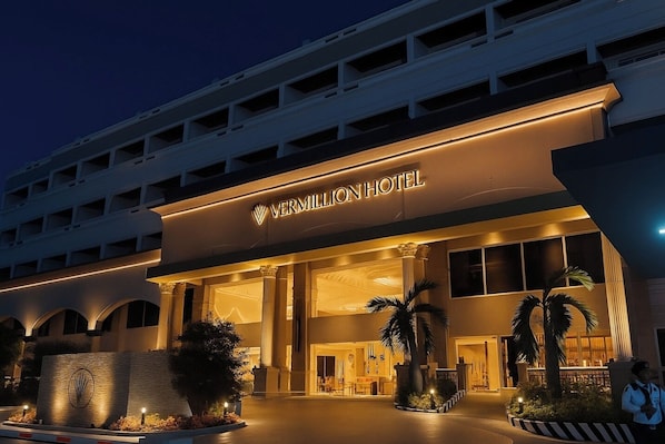 The Vermillion Hotel entrance with a modern design, featuring a large illuminated sign, a covered entrance, and a landscaped area with palm trees. - Vermillion Hotel (Iloilo)