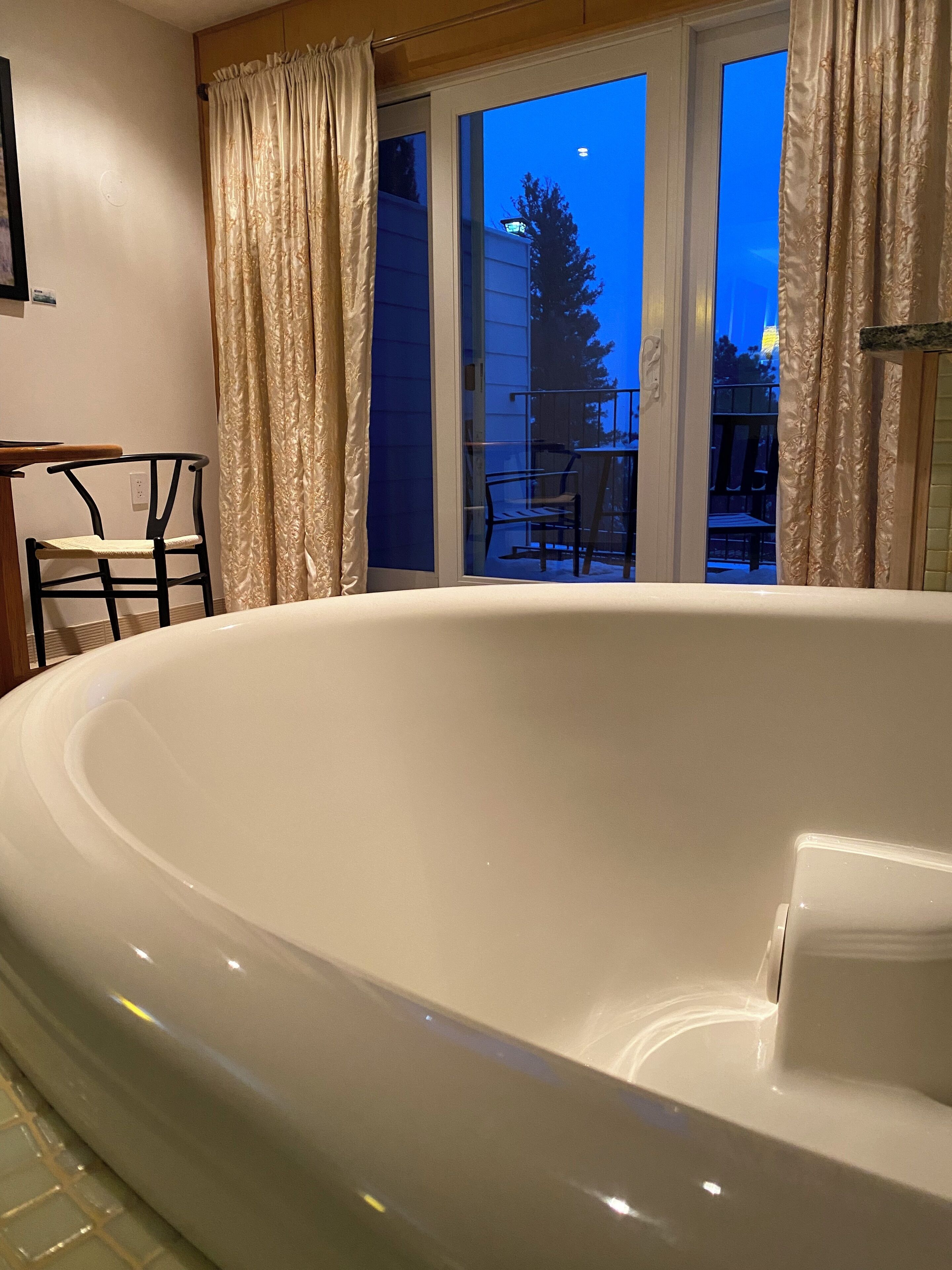 Une salle de bain moderne avec une grande baignoire, un fauteuil et une fenêtre avec des rideaux.