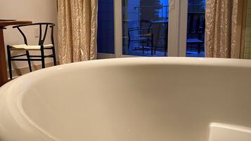 Une salle de bain moderne avec une grande baignoire, un fauteuil et une fenêtre avec des rideaux.
