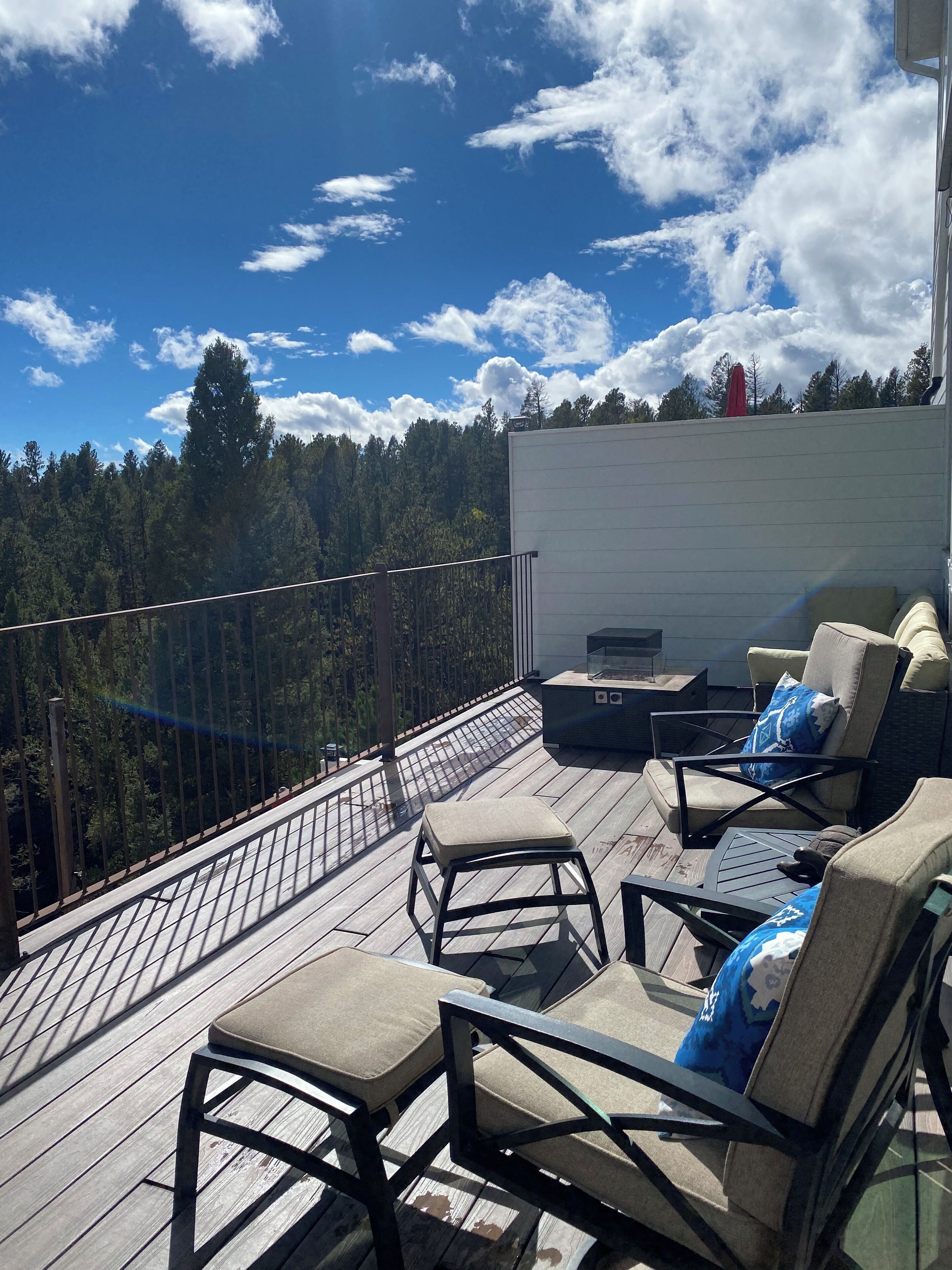 A deck with outdoor furniture, a glass table, and a view of a forest.