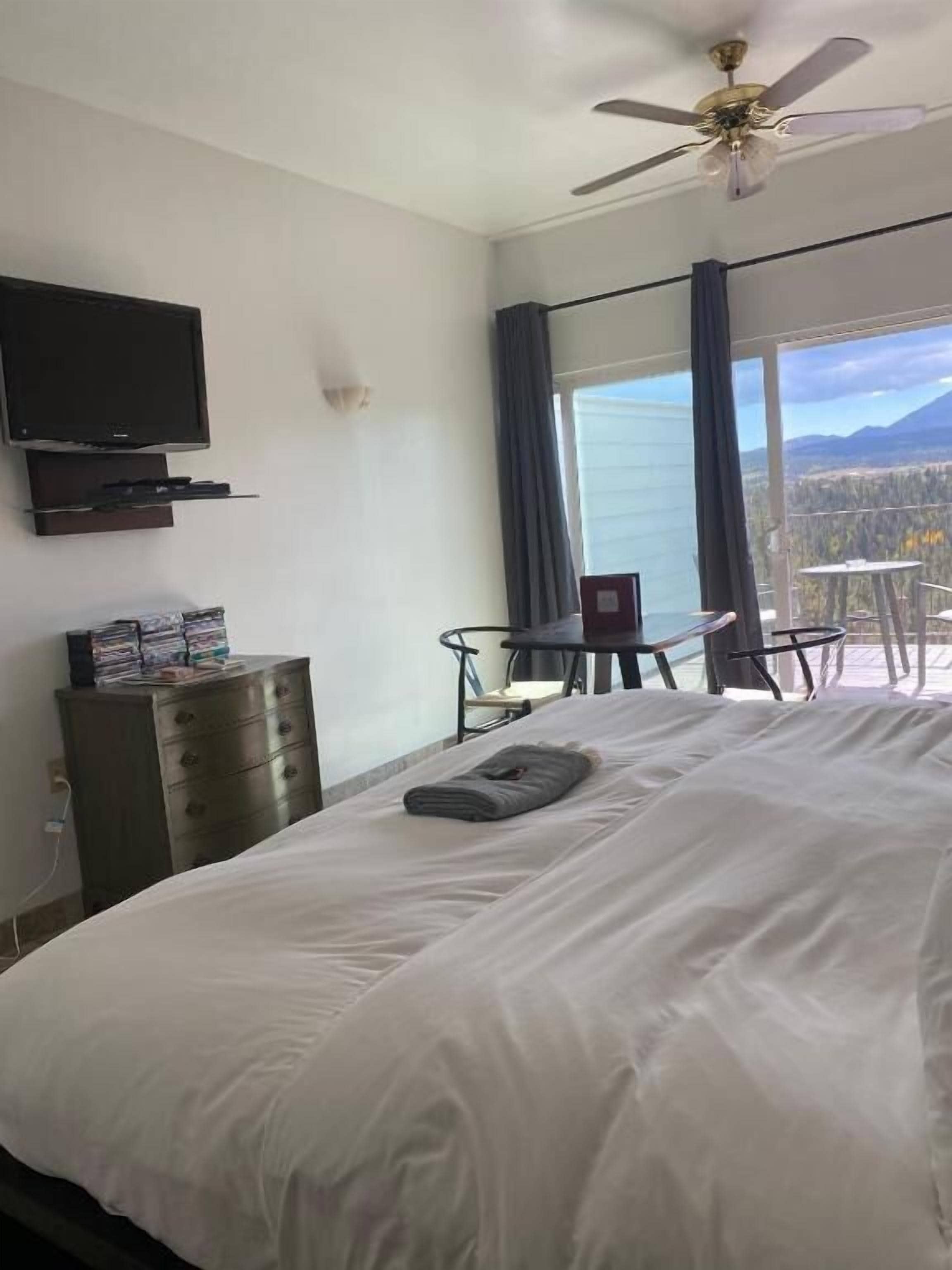 A hotel room with a bed, a television, a dresser, and a balcony with a table and chairs.