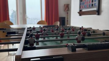 Una mesa de fútbol de mesa en una habitación con ventanas, cortinas rojas y un ventilador de techo.