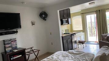 A bedroom with a bed, a TV, a small desk, and a kitchenette.