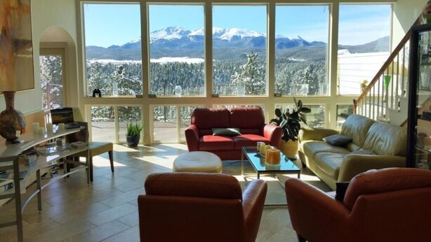 A spacious living room with a large window overlooking a mountainous landscape. - Pikes Peak Paradise Bed and Breakfast (Woodland Park)