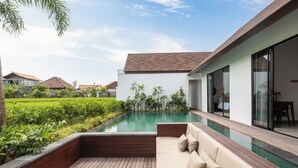 Ett modernt utomhusområde med pool, ett trädäck, en beige soffa och frodig grönska.