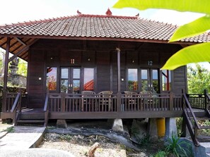 A wooden building with a tiled roof, numbered rooms 11 and 12, and a covered porch with chairs. - Sunrise Cottage Villa Lembongan (Lembongan Island)