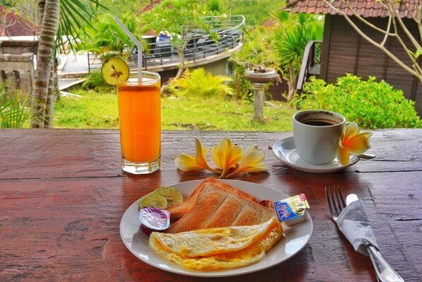 A meal with toast, eggs, and a drink on a wooden table with a tropical garden view.