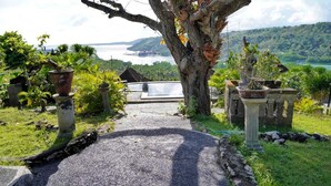 Un sendero que lleva a una casa tradicional, con vista a un cuerpo de agua y colinas.