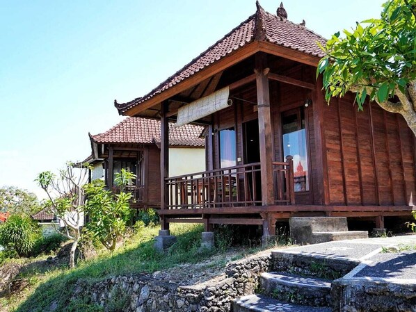 A traditional wooden house with a tiled roof, a balcony, and a stone pathway leading to the entrance.