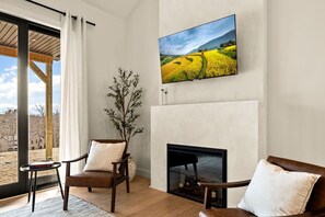 A living room with a fireplace, a television mounted above it, and a view of a field through the window.