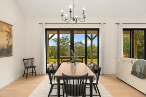 A dining area with a large table, chairs, a chandelier, and a view through glass doors to an outdoor garden.