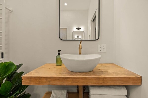 A bathroom with a wooden vanity, a white sink, a mirror, and a green soap dispenser.