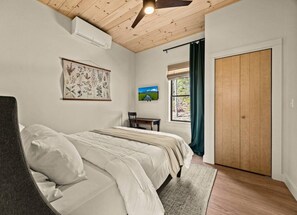 A bedroom with a bed, a desk, a chair, a window with curtains, and a wooden door.