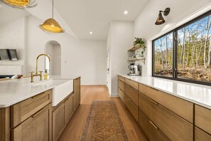 A modern kitchen with a central island, wooden cabinets, and a large window offering a view of trees.