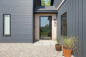 A modern building with a grey exterior, a black-framed door, and a small window. There are two potted plants in front of the door.