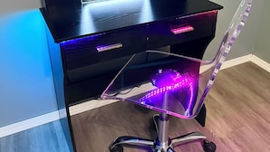 Un moderno tocador con espejo, iluminado por luces LED, y una silla de oficina transparente.