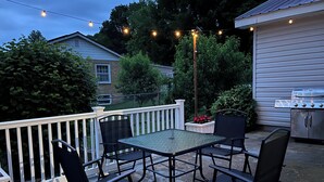 Un patio al aire libre con una mesa, sillas, una parrilla y luces colgantes.