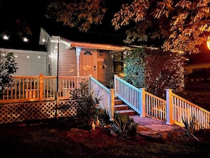 Stunning entrance with a beautifully lit front door, wooden staircase, and lush gardens.
