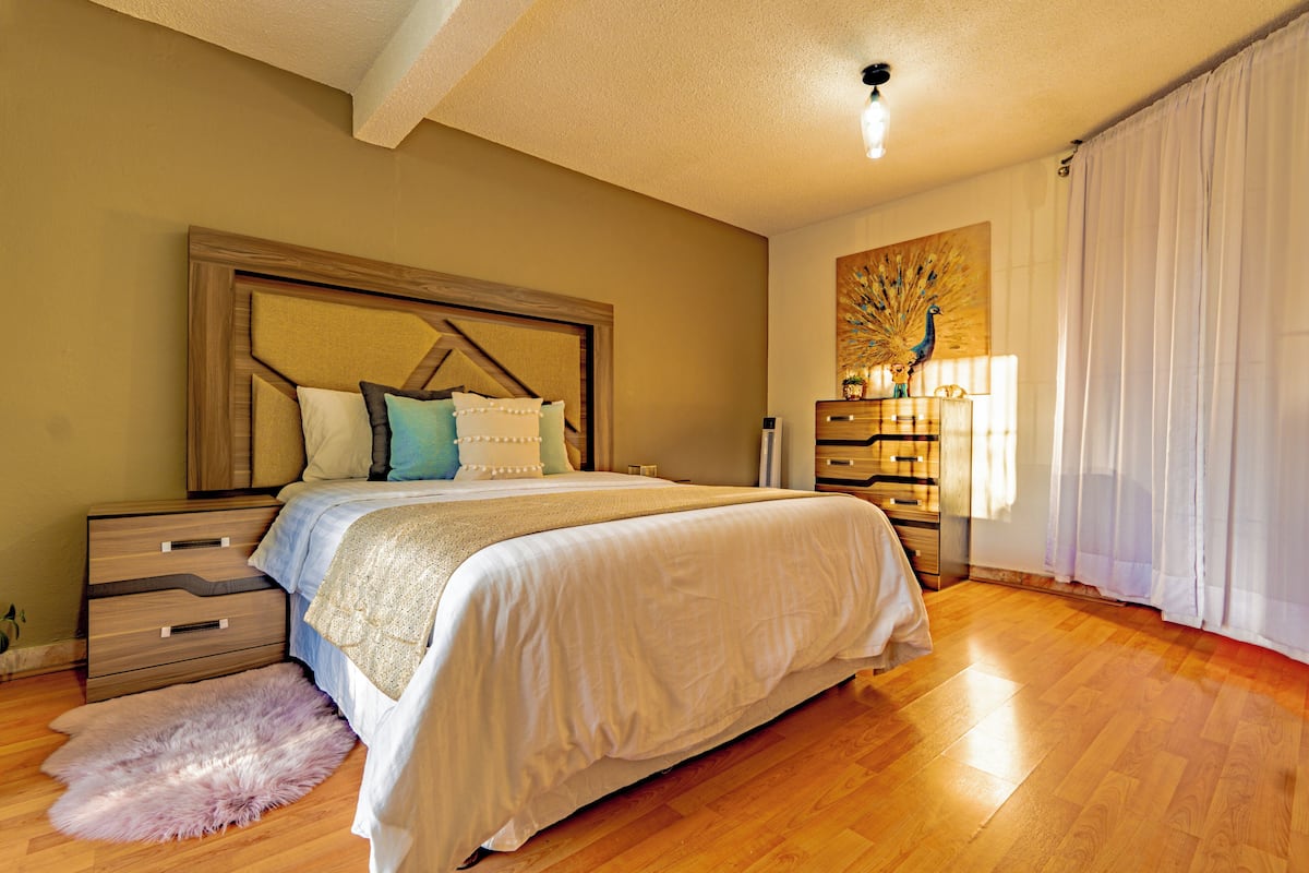 A bedroom with a large bed, wooden nightstands, a fluffy rug, and a decorative tree painting.