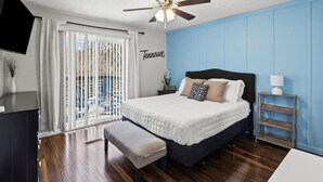 A bedroom with a bed, a bench, a nightstand, a TV, and a ceiling fan.