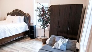 A bedroom with two beds, a dark wardrobe, a potted plant, and a window. - Cozy & Stylish One-Bedroom Apartment Near Downtown Moncton (Moncton)