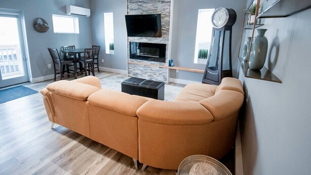A modern living room with a sectional sofa, a fireplace, a dining area, and a large window. - Cozy & Stylish One-Bedroom Apartment Near Downtown Moncton (Moncton)