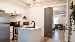 A modern kitchen with a central island, wooden flooring, and a geometric ceiling design. - Cozy & Stylish One-Bedroom Apartment Near Downtown Moncton (Moncton)