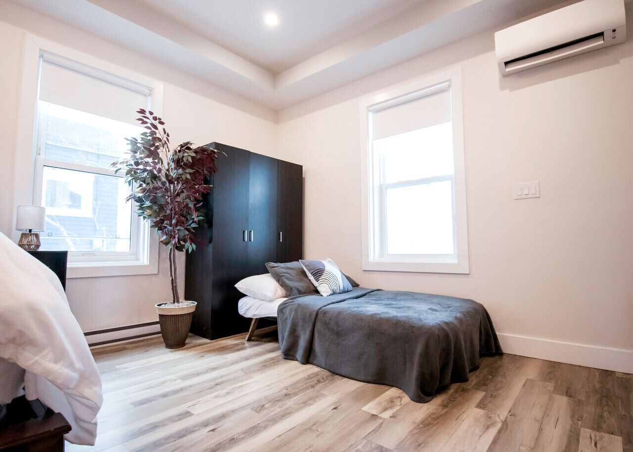 Quarto com cama, guarda-roupa, planta em vaso e janela.