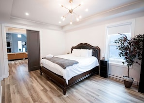 A bedroom with a wooden bed, a potted plant, and a window with blinds.