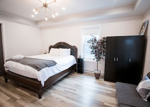 Ein Schlafzimmer mit einem hölzernen Bett, einem dunklen Kleiderschrank, einem grauen Sofa und einer Topfpflanze.