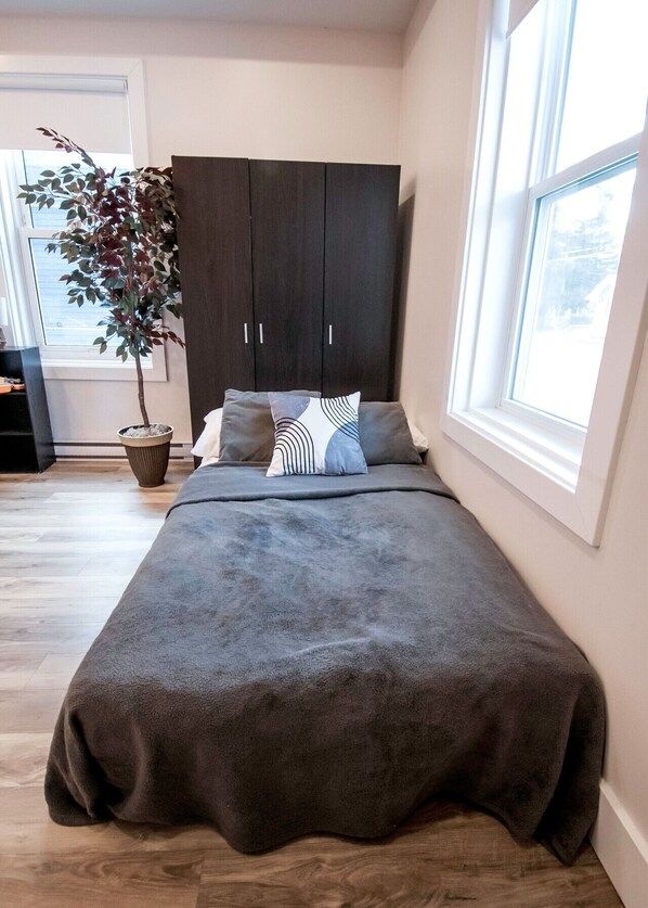 Un dormitorio con cama, armario oscuro, planta en maceta y ventana grande.