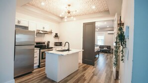 A modern kitchen with white cabinetry, a central island, and a geometric ceiling design. - Cozy & Stylish One-Bedroom Apartment Near Downtown Moncton (Moncton)