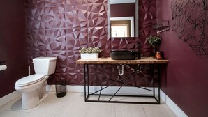 A bathroom with a geometric-patterned wall, a white toilet, a wooden vanity with a mirror, and a black sink. - Cozy & Stylish One-Bedroom Apartment Near Downtown Moncton (Moncton)