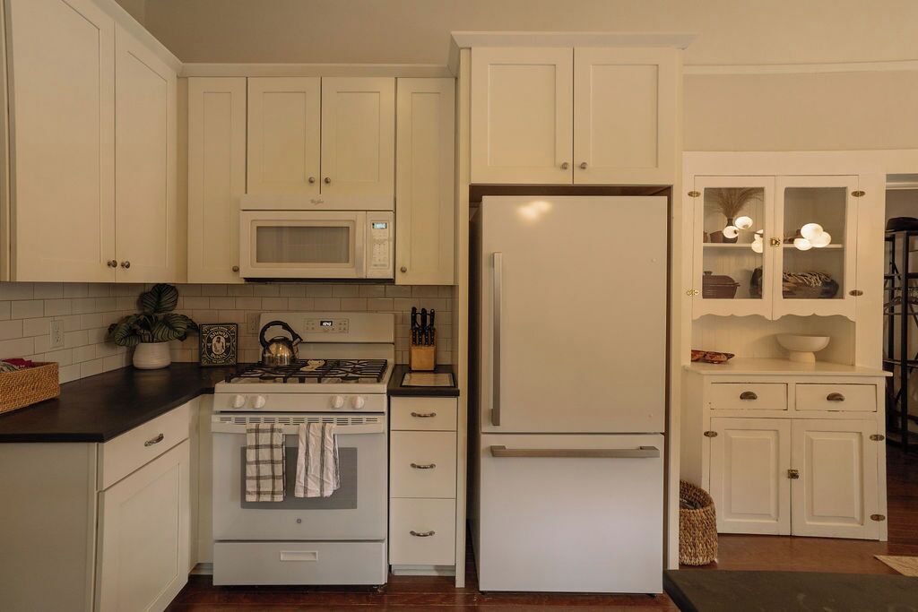 A kitchen with white cabinets, a stove, a microwave, and a refrigerator.
